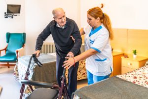 Home health aide helps an elderly man walk